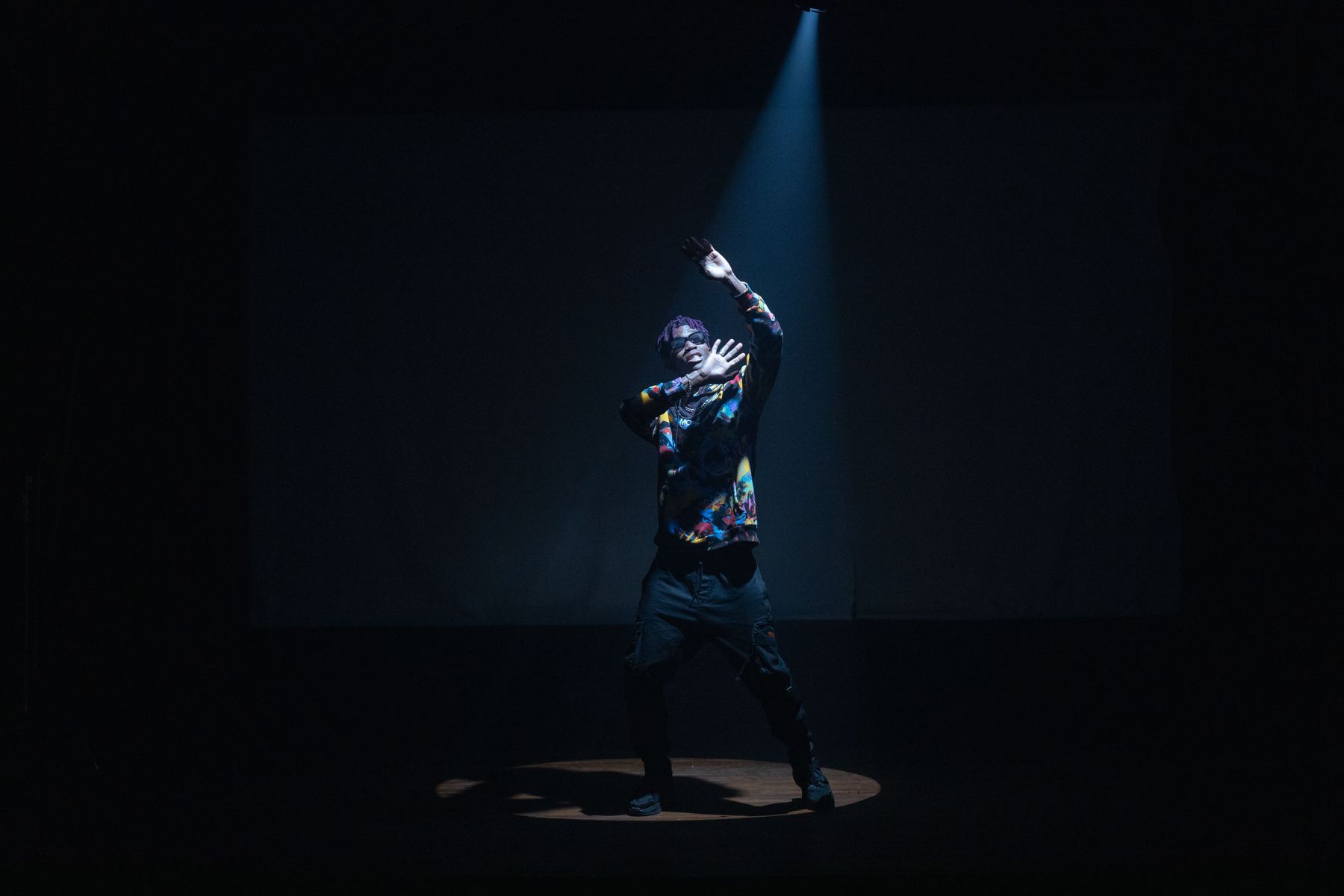 A dancer alone on a dark stage, caught in a single beam of light from above